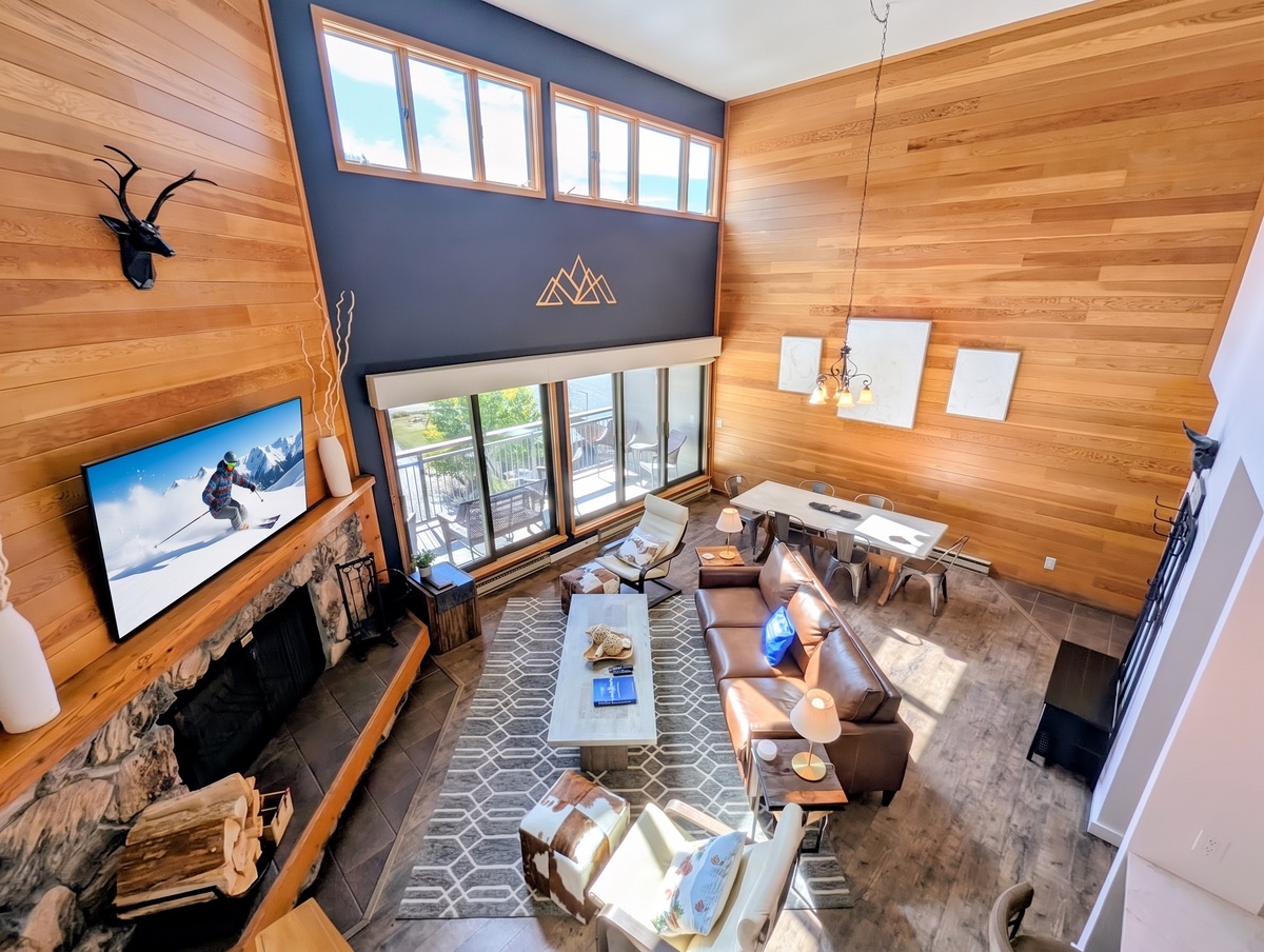Soaring living space with rich wood-paneled walls, vaulted ceilings, and abundant natural light. Relax in plush leather seating by the stone fireplace, step onto the balcony for mountain air, and dine together after a day of adventure.