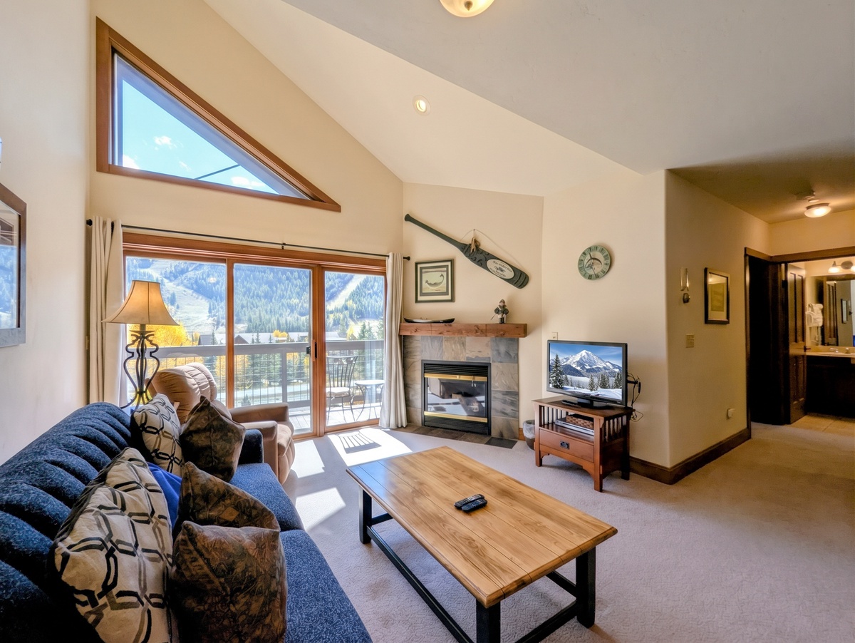 Sunlight pours through floor-to-ceiling windows into your spacious mountain retreat, where vaulted ceilings and a cozy fireplace create the perfect après-ski haven with stunning alpine views.