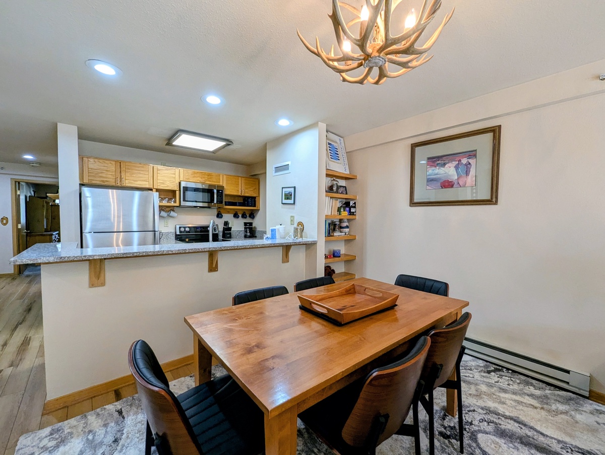 Gather around this inviting dining area where your group can share meals beneath a striking antler chandelier. The open layout connects you to the full kitchen, making it easy to prepare and serve your favorite dishes together.
