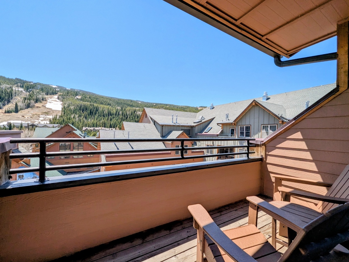 Private deck overlooking ski slopes and forested mountains, with comfortable seating and retractable awning for sun-drenched relaxation during summer mountain adventures.
