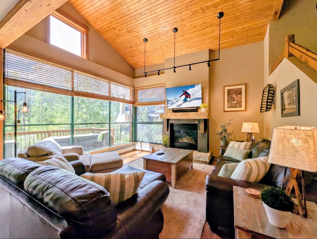 Sink into plush sofas by the fireplace while natural light pours through expansive windows framing peaceful forest views—your perfect mountain escape.