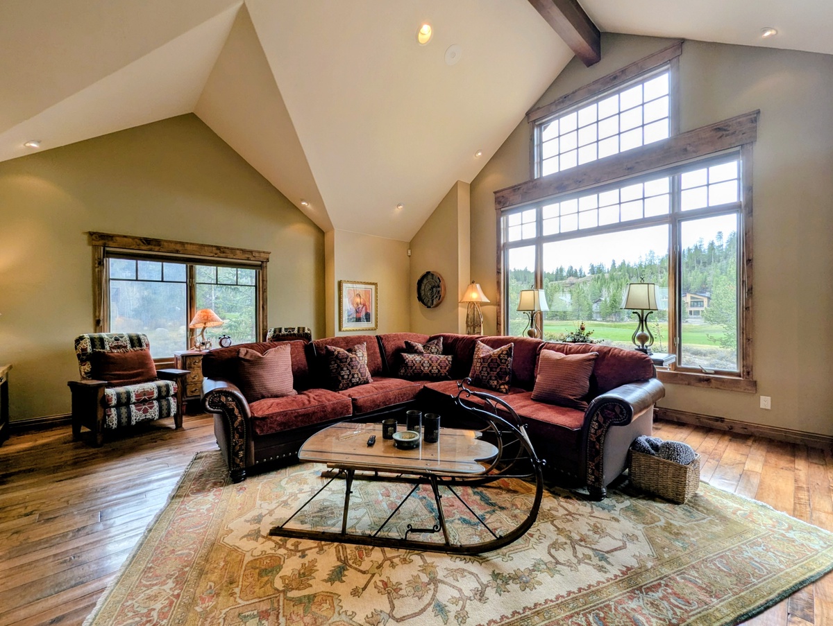 Relax in your spacious living room with soaring vaulted ceilings and warm natural light streaming through oversized windows. Sink into plush seating and enjoy peaceful views of the surrounding forest and meadow.
