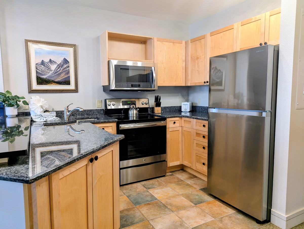 Your fully equipped kitchen features modern stainless steel appliances, granite countertops, and warm natural wood cabinetry—perfect for preparing meals during your stay.