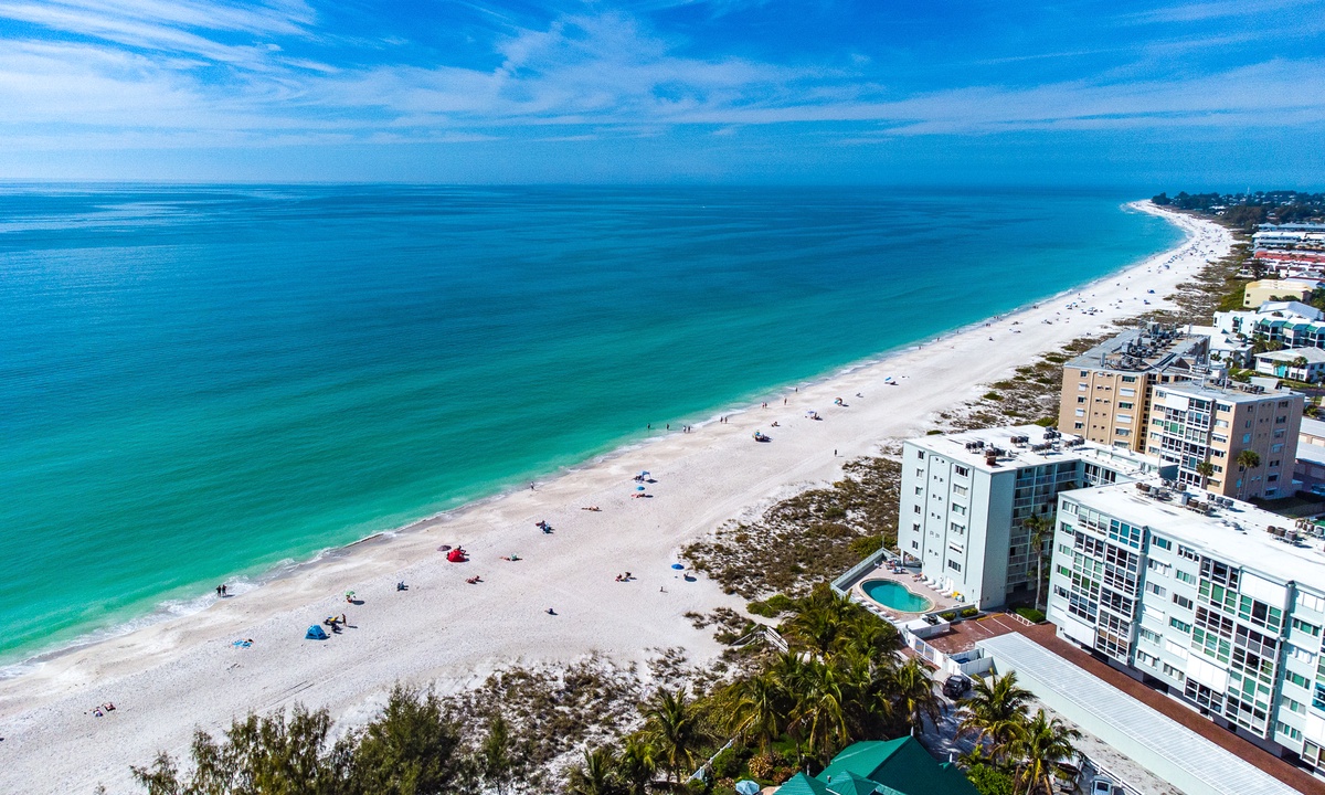 Arial shot of the beach on Anna Maria Island, in the right of the frame are vacation rentals in large complexes available for rent.