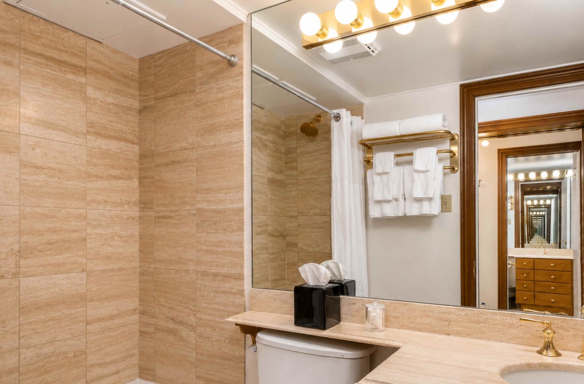 Step into your sleek bathroom featuring warm travertine tiles, gleaming fixtures, and plush towels waiting just for you.