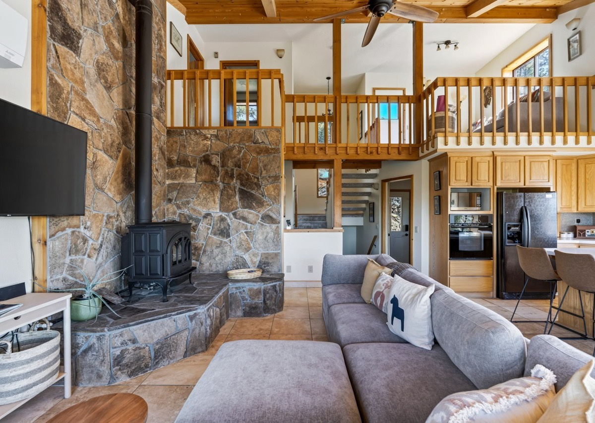 Relax in this inviting open-concept living space with soaring wood-beamed ceilings, a striking stone fireplace, and cozy seating that invites you to unwind in mountain-chalet style.