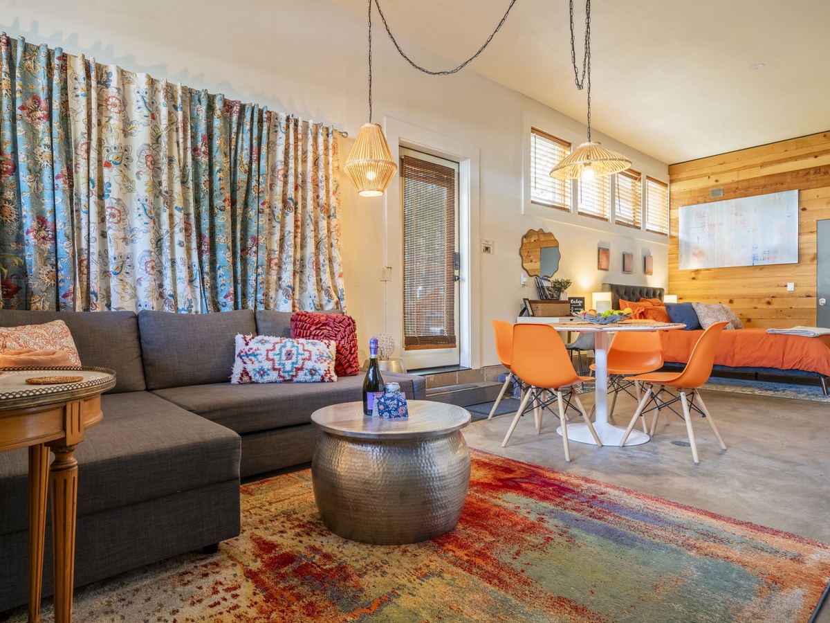 Your open-plan retreat blends vibrant living, dining, and sleeping spaces with warm wood accents, woven pendant lights, and colorful textiles—a cozy, eclectic haven for relaxation.