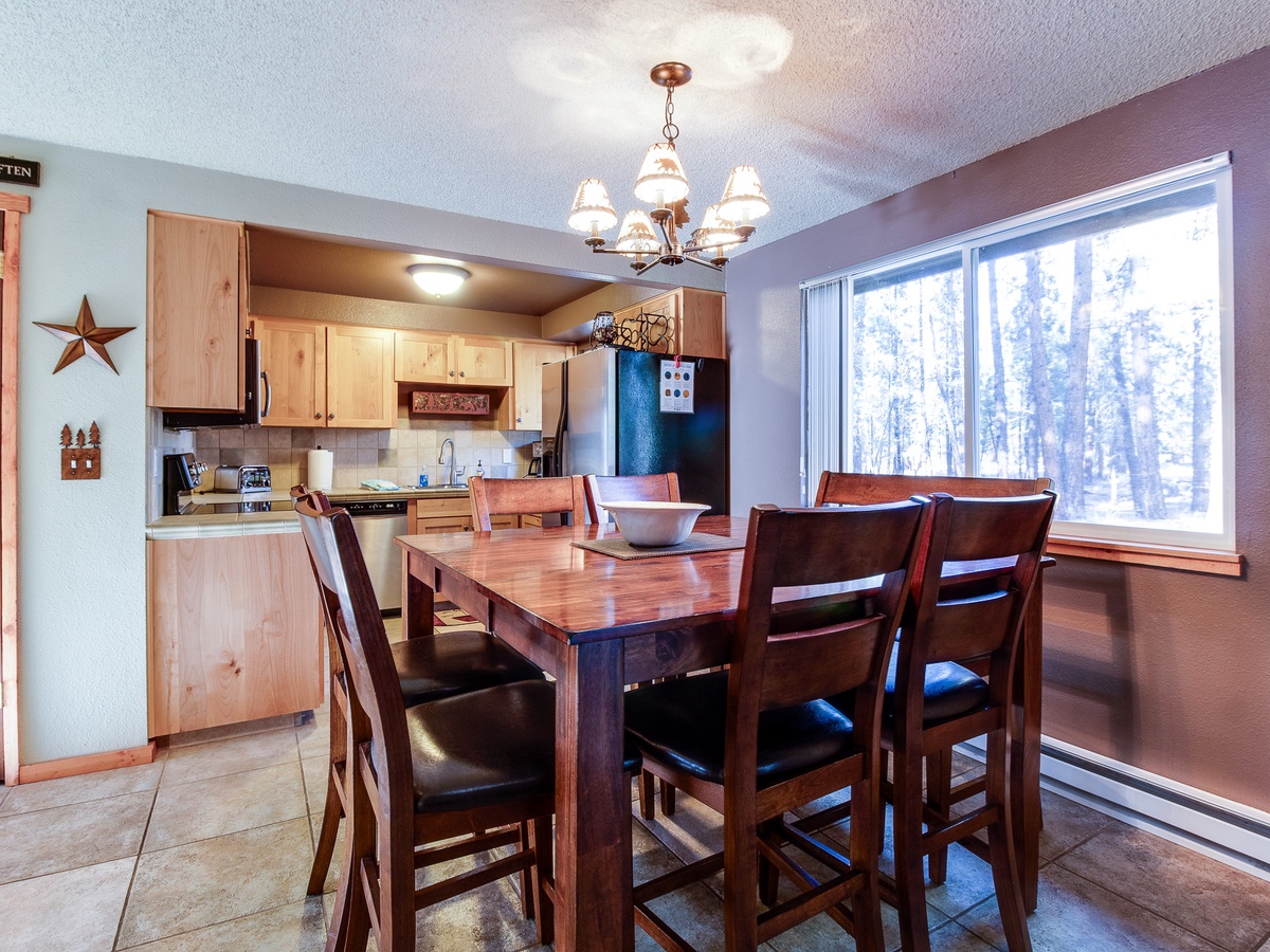 Gather around this inviting dining table with snowy forest views just beyond the window, perfect for cozy meals after a day of mountain adventure.