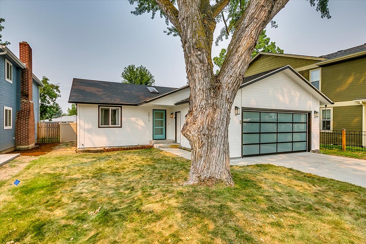 Modern ranch-style home with glass garage door sits in a quiet residential neighborhood, featuring mature shade trees and contemporary design.