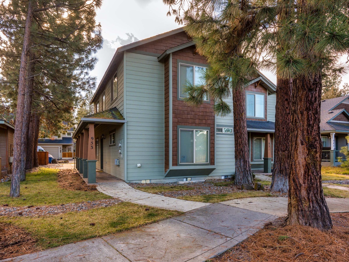 A modern two-story rental home nestled among towering pine trees in a peaceful residential neighborhood.