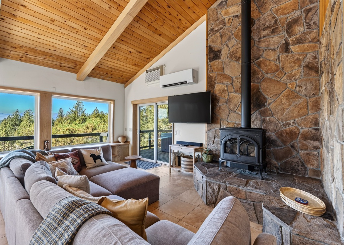 Settle into your cozy living room where vaulted wood ceilings and a stunning stone fireplace create the perfect mountain retreat. Through expansive windows, you'll enjoy natural light and peaceful views of the surrounding pines.