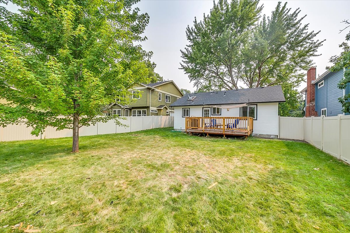 Charming single-story home with spacious backyard featuring wooden deck and mature shade trees in quiet residential neighborhood.