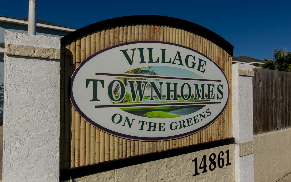 Property entrance sign for Village Townhomes on the Greens with clear address marking and decorative stone and bamboo design elements.