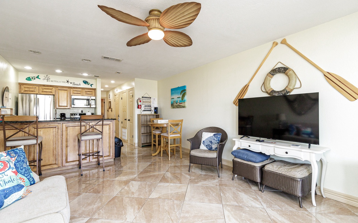 Unwind in your bright, coastal-themed living space featuring charming nautical touches, a ceiling fan, and open-concept kitchen perfect for vacation relaxation.
