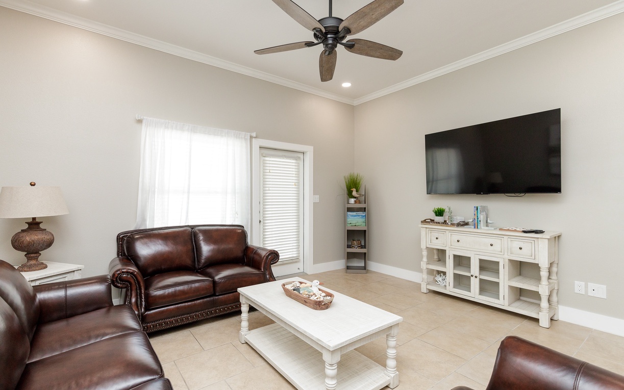 Relax in your spacious living room with plush leather seating, modern entertainment center, and cooling ceiling fan for ultimate comfort.