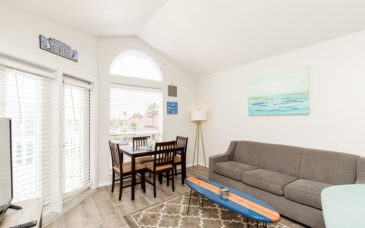 Unwind in your coastal-themed living space with comfy seating, beach-inspired decor, and abundant natural light streaming through shuttered windows.