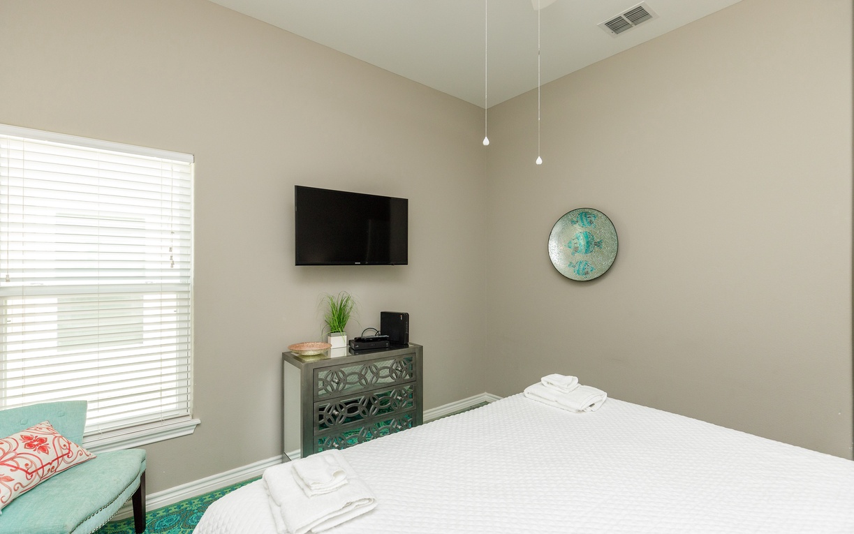 Settle into your peaceful bedroom where soft light flows through venetian blinds and modern comfort awaits with plush towels.