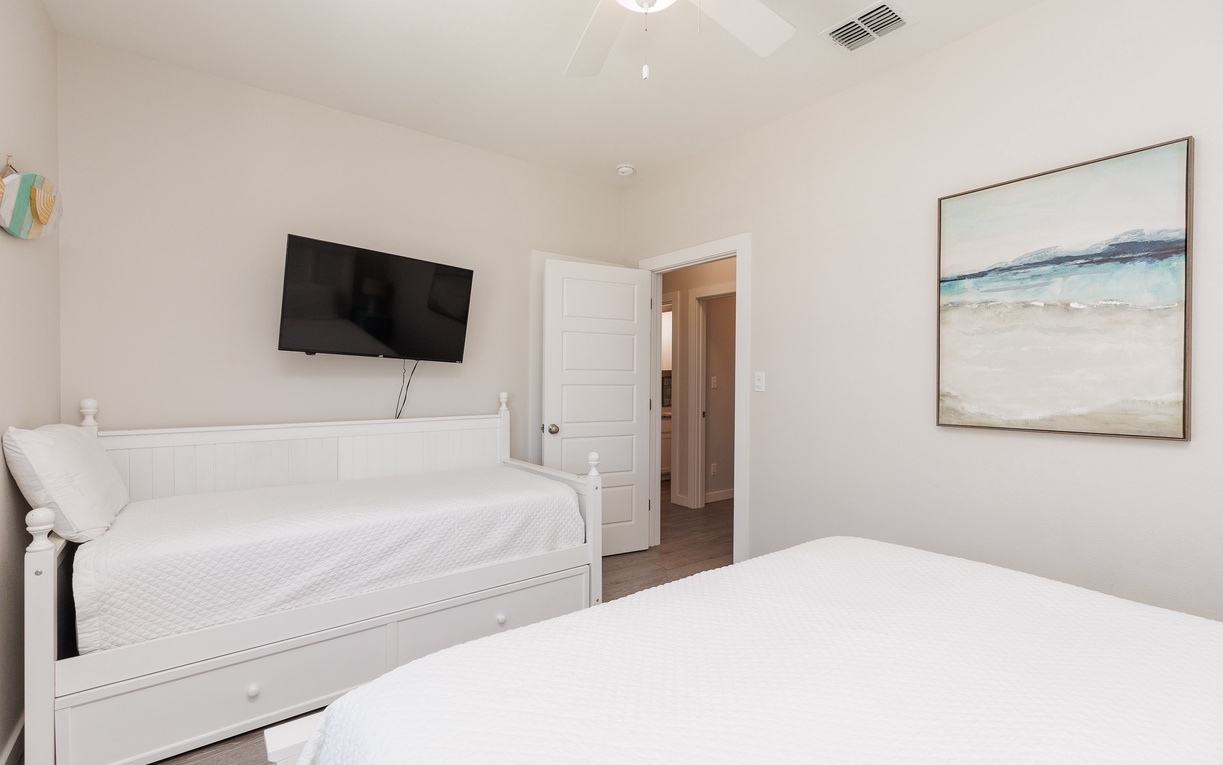 Relax in your bright bedroom with twin beds, wall-mounted TV, and coastal artwork creating a peaceful atmosphere.