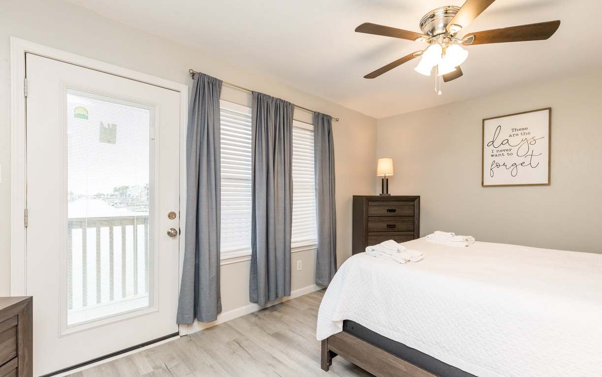 Drift off in this peaceful bedroom with plush linens, gentle ceiling fan, and natural light streaming through your private balcony door.