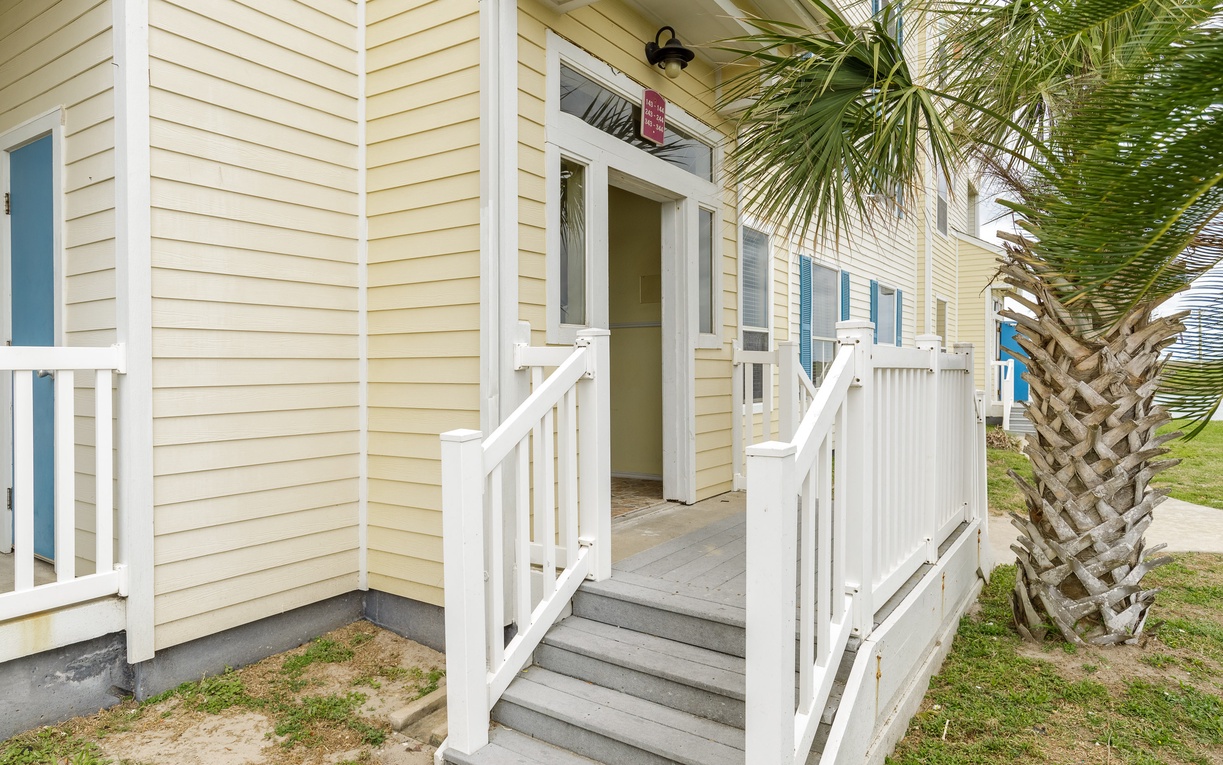 Coastal cottage entrance with charming blue shutters and tropical palm tree creating a welcoming beachside retreat.
