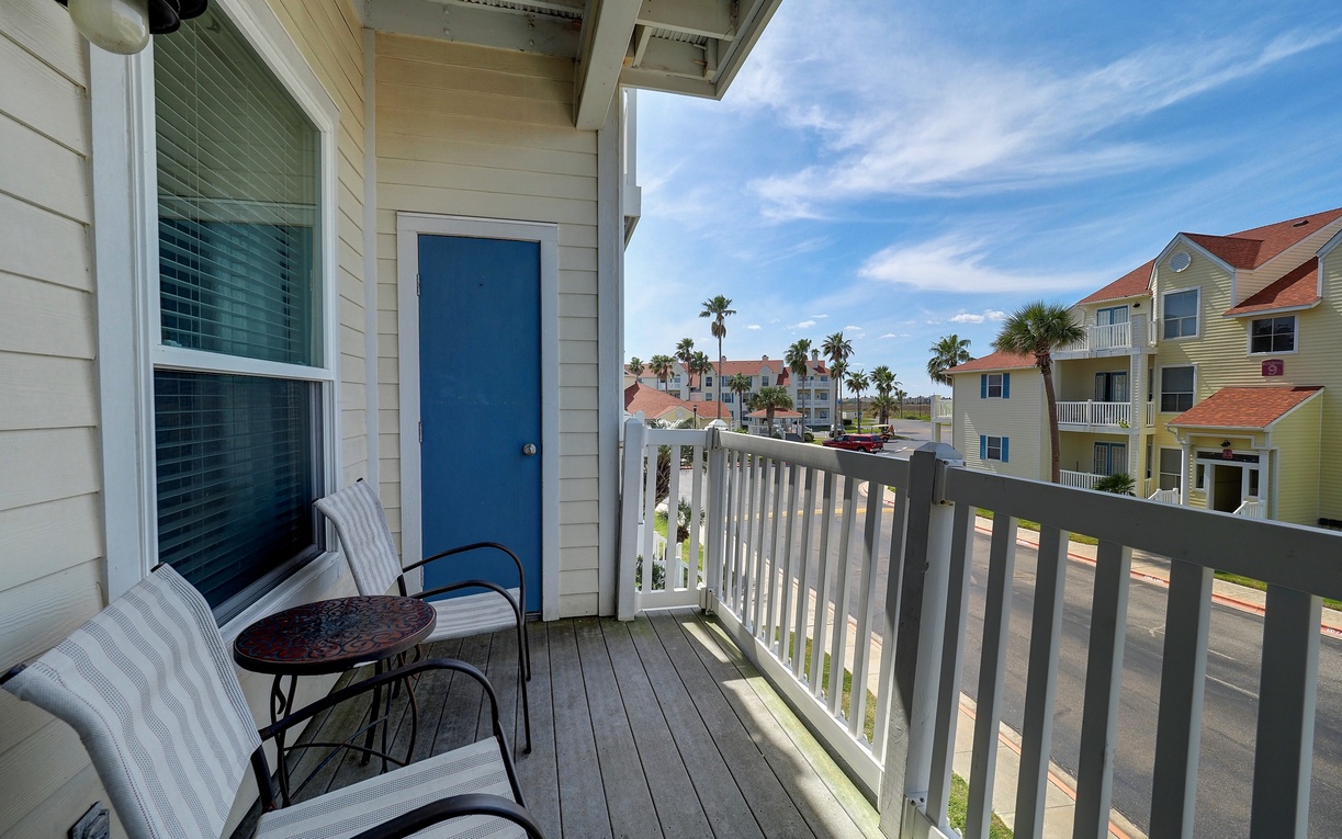 Enjoy your morning coffee on this sunny balcony with comfortable seating and tropical views of colorful coastal buildings.