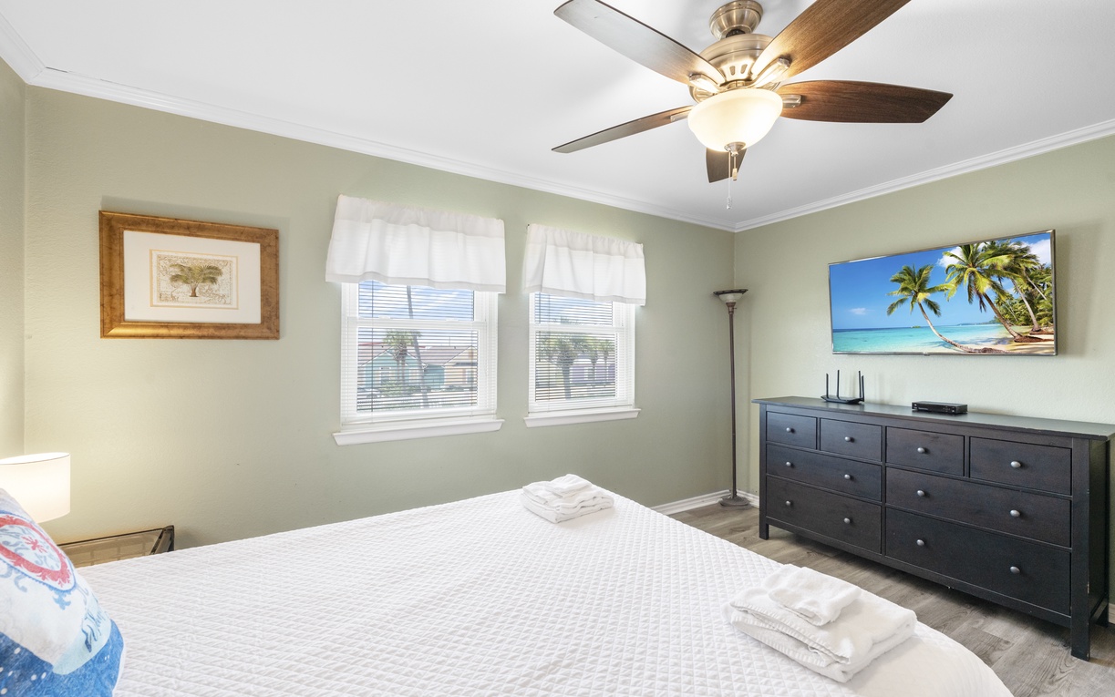 Relax in your peaceful bedroom with coastal charm, ceiling fan comfort, and tropical views on the wall-mounted TV.