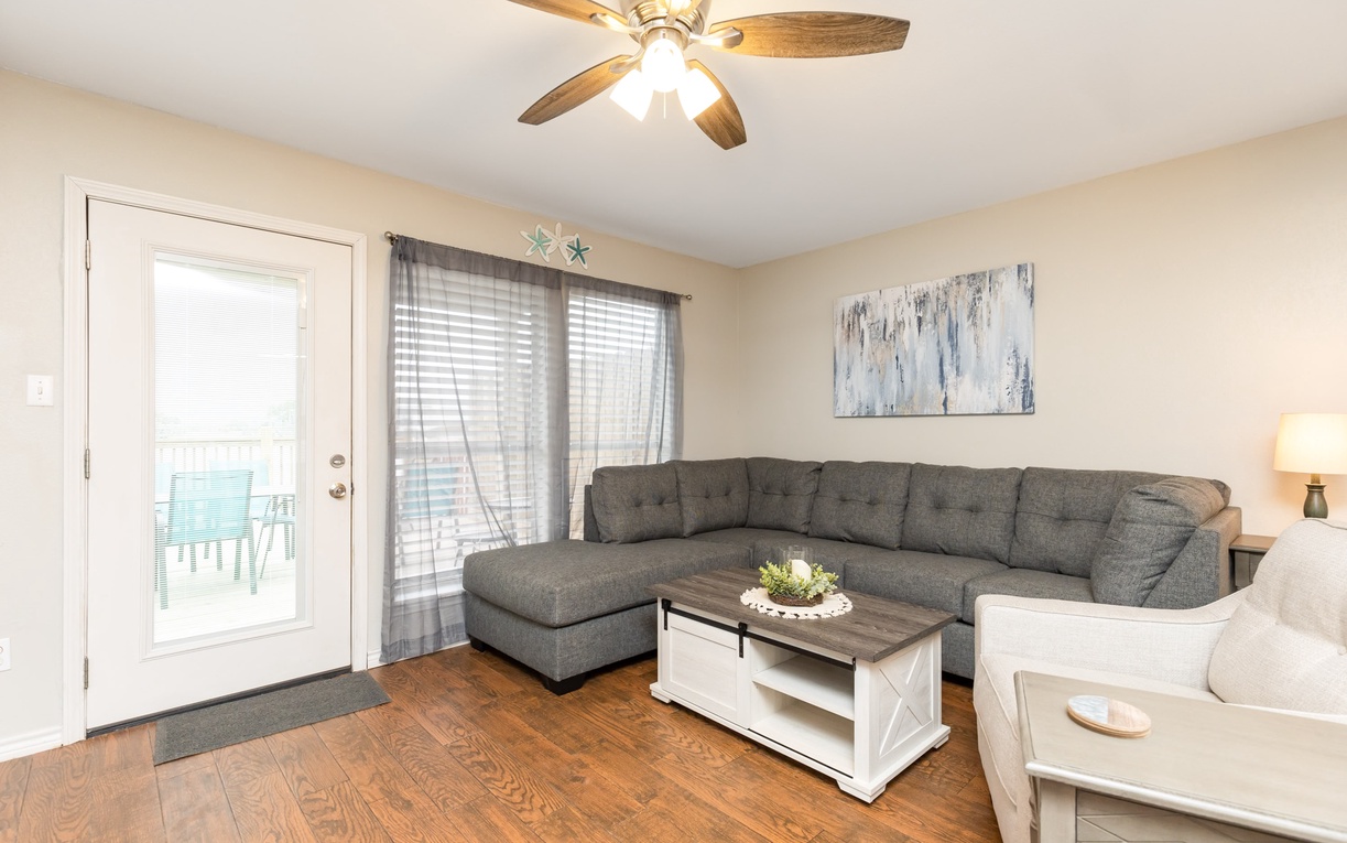 Relax in your bright living room with plush sectional seating, warm wood floors, and a gentle ceiling fan breeze.