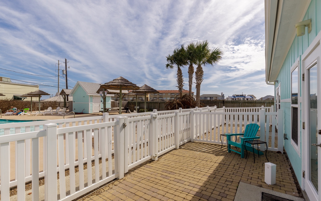Step onto your private patio with turquoise chairs where palm trees and pool views create your perfect coastal retreat.
