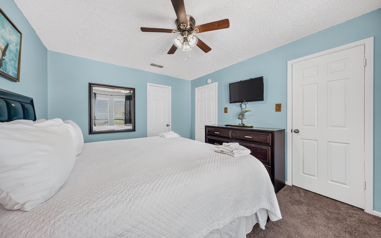 Unwind in your serene bedroom with soft blue walls, a plush bed dressed in crisp linens, and a ceiling fan to keep you cool and comfortable throughout your stay.