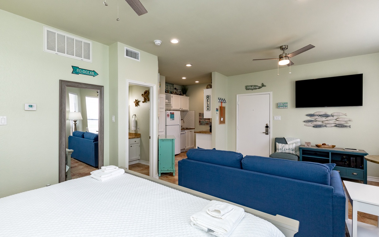 Relax in your bright studio with cozy blue sofa, fully equipped kitchen, and modern amenities—perfect for unwinding after beachside adventures.