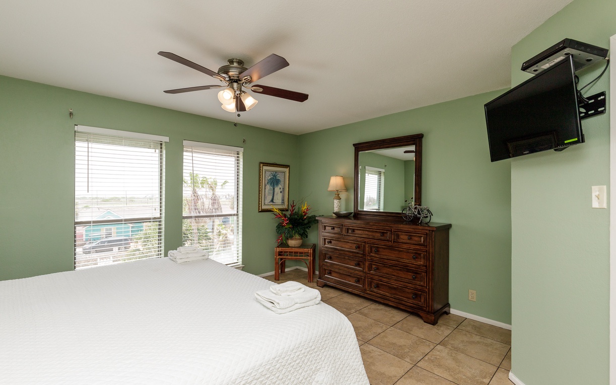 Relax in your peaceful bedroom with soothing sage walls, a ceiling fan for comfort, and entertainment on the mounted TV.