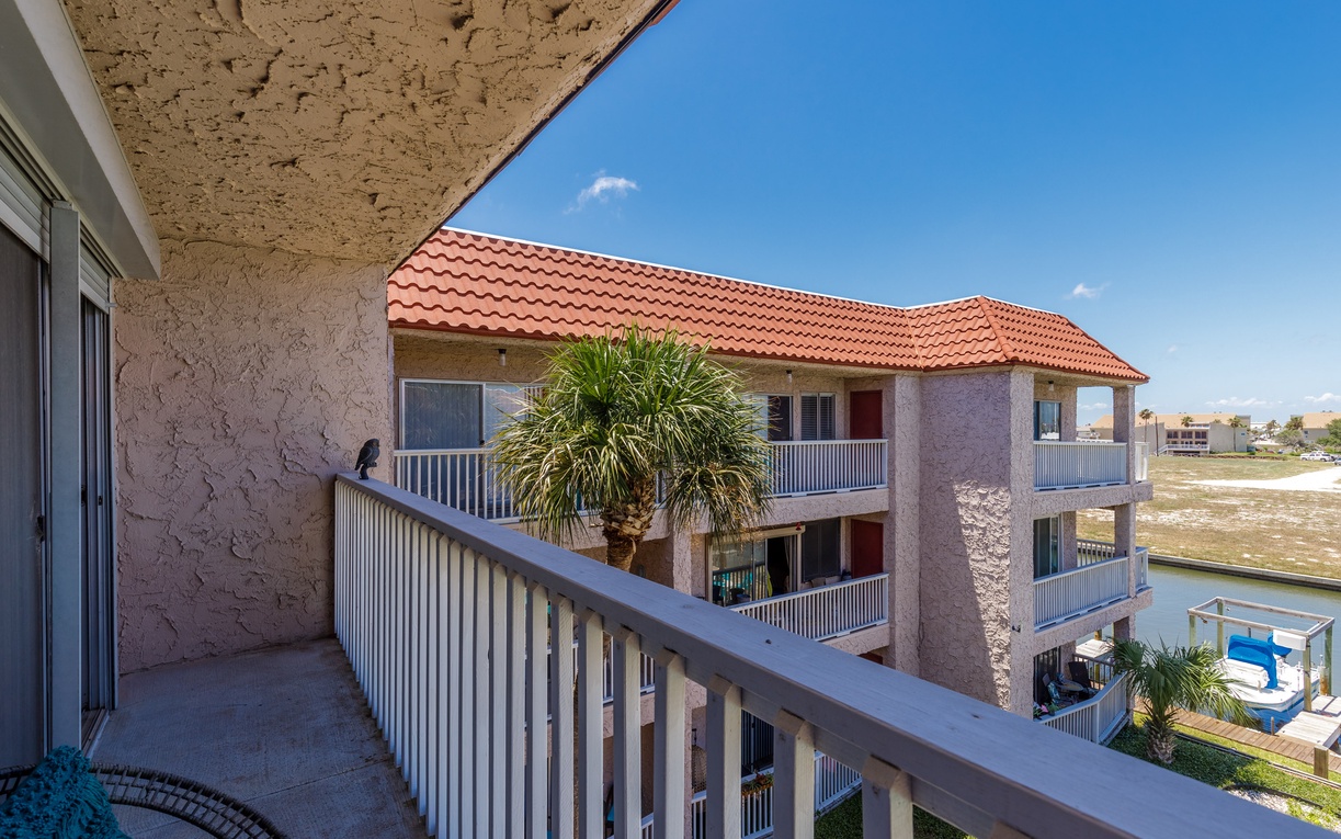 Mediterranean-style building with red tile roofing in a sunny residential development with open land views beyond.