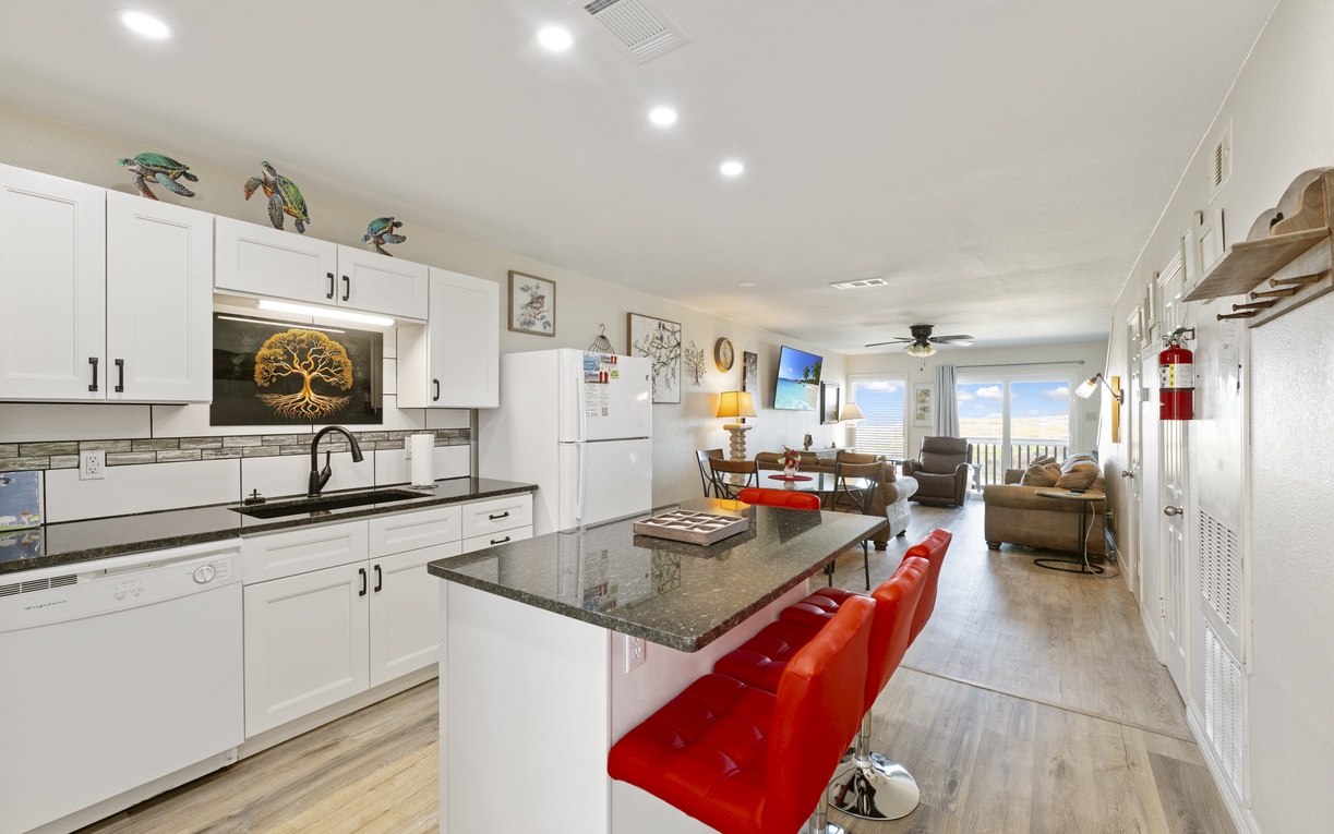 Your bright, open-plan living space flows seamlessly from kitchen to lounge, with vibrant red bar stools and ocean views awaiting.