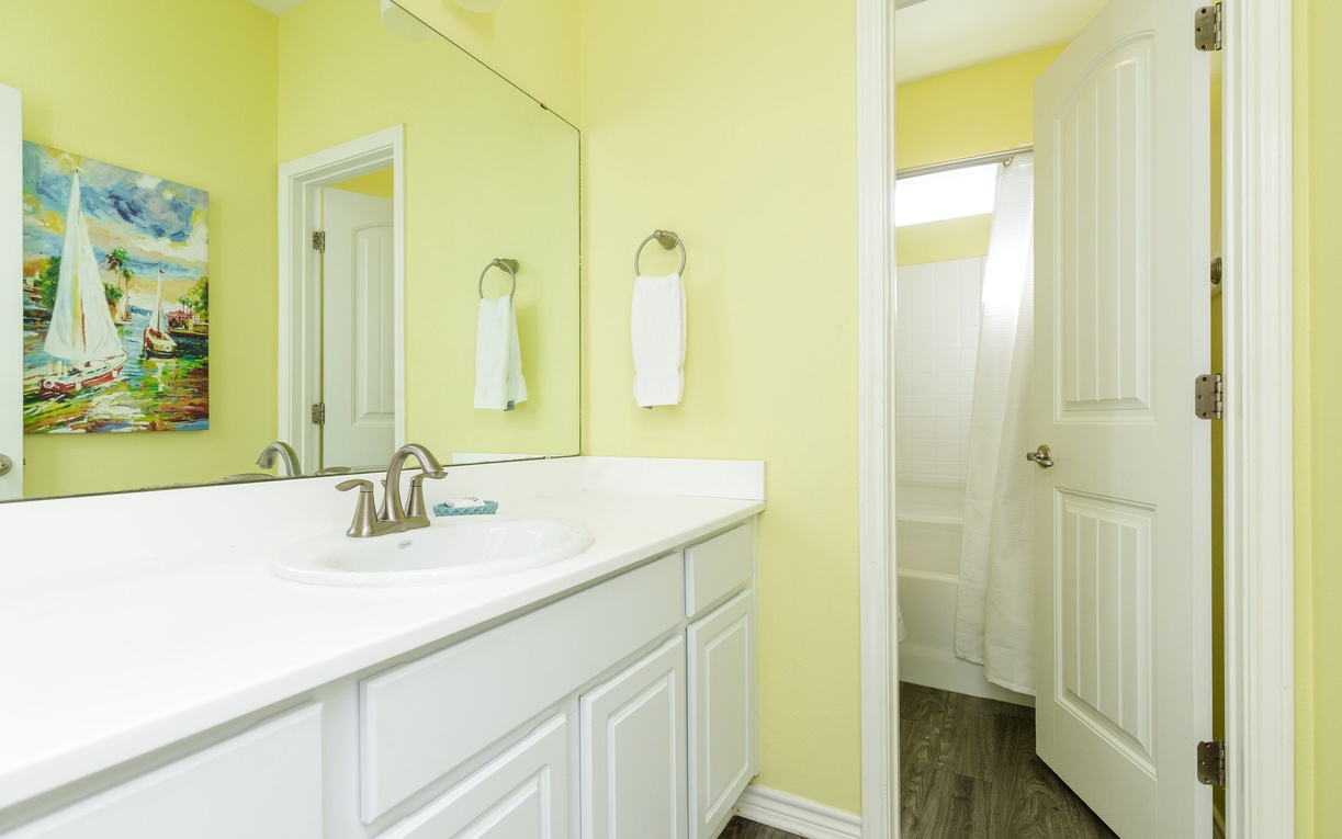 Refresh in your cheerful yellow bathroom with clean white vanity, fresh towels, and convenient separate shower.