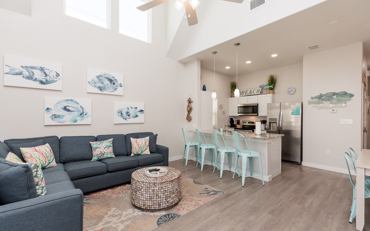 Relax in your bright, beach-themed living space with soaring ceilings, coastal artwork, and a fully equipped kitchen perfect for vacation meals.