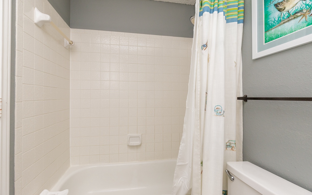 Step into your private bathroom featuring a spacious tub-shower combo with coastal-themed curtains and fresh towels waiting for you.