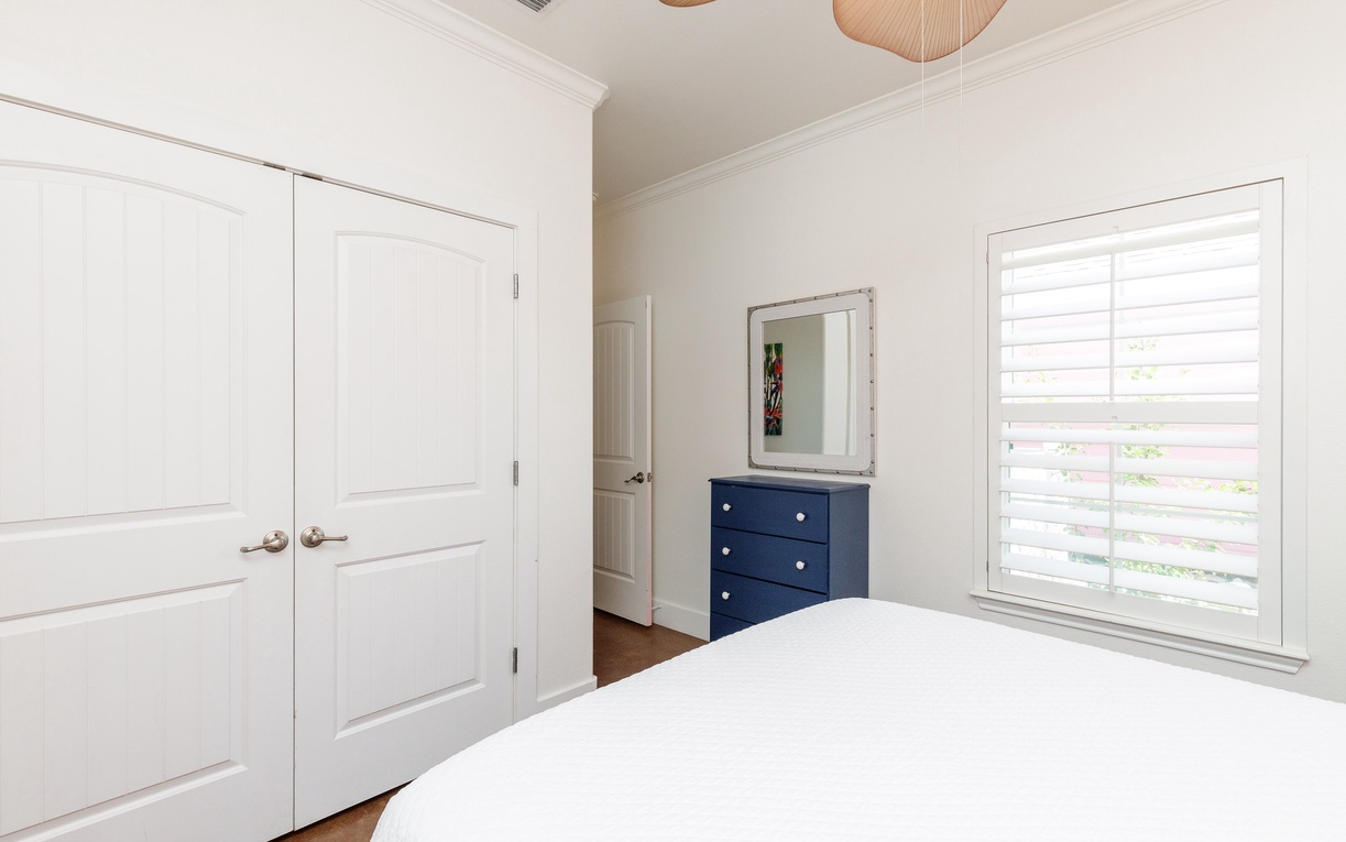 Your bright bedroom features crisp white linens, stylish navy accents, and natural light streaming through plantation shutters for peaceful mornings.