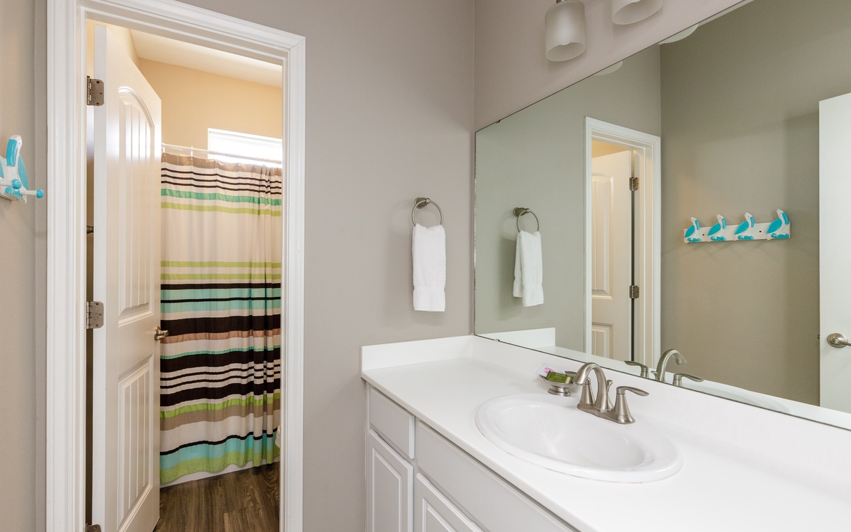 Refresh in your bright, modern bathroom with colorful striped shower curtain, white vanity, and cheerful turquoise accents.