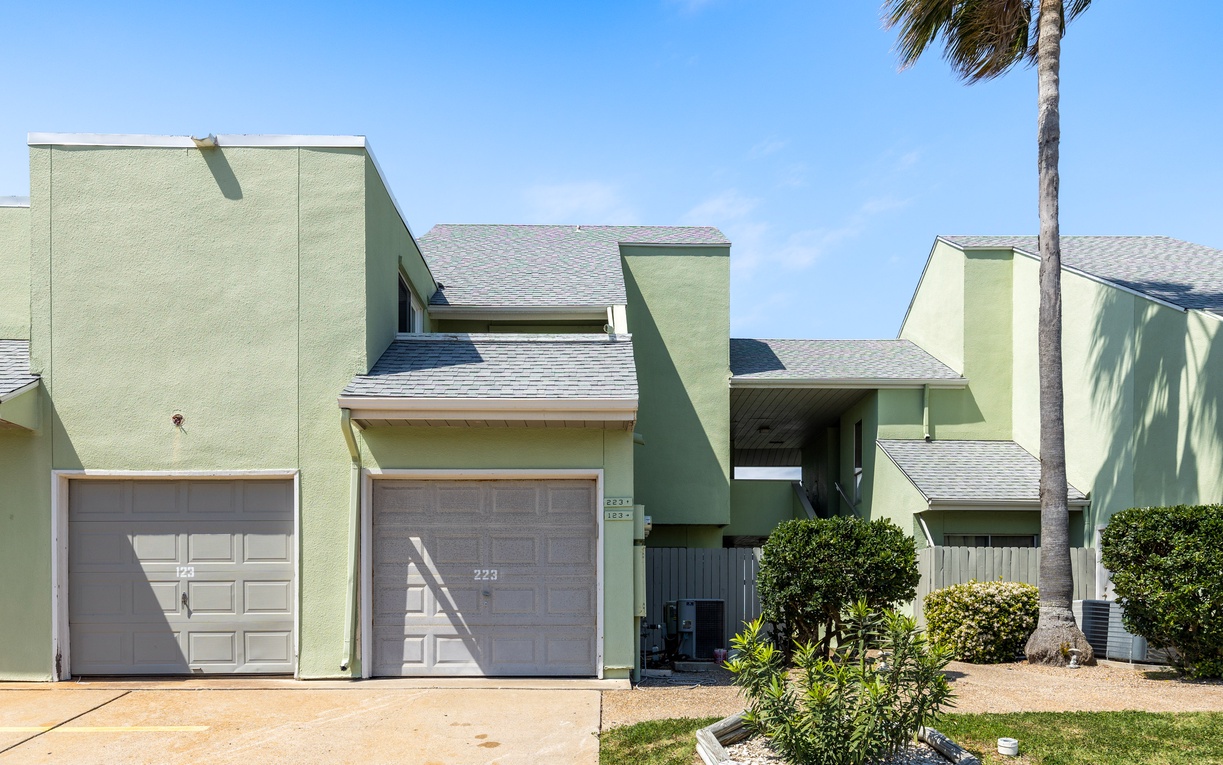Modern green townhome complex with palm trees and manicured landscaping in a sunny coastal setting.