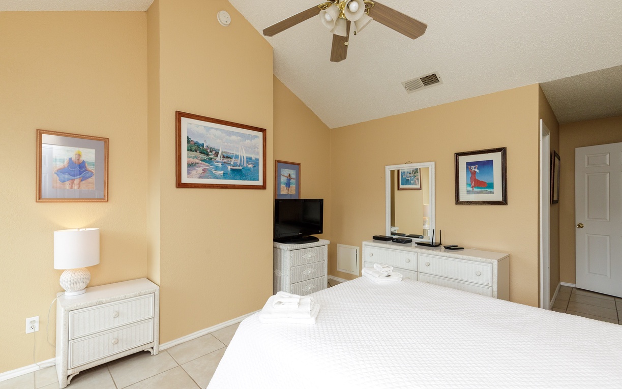 Your serene bedroom features coastal artwork, vaulted ceilings, and white wicker furniture creating a peaceful retreat for restful nights.