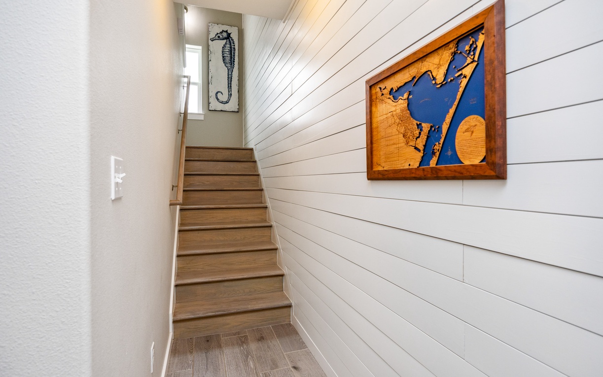 Ascend the charming wooden stairs where coastal artwork welcomes you to your next level of relaxation.