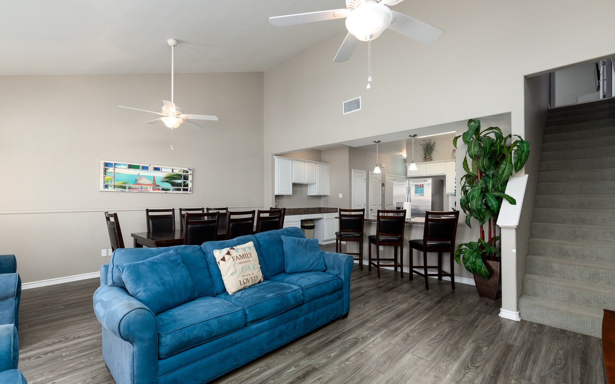 Relax in your spacious open-concept living area with comfortable blue seating, modern kitchen, and elegant dining space perfect for group gatherings.