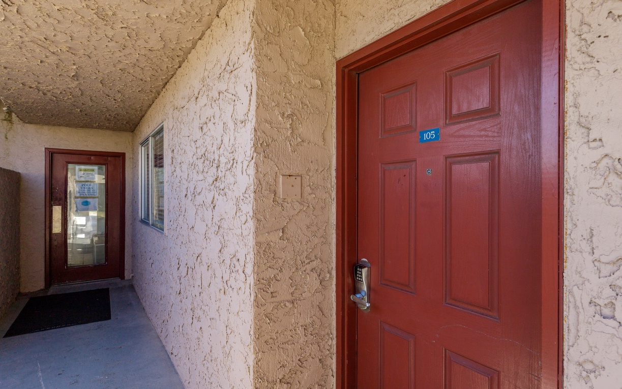 Your private entrance awaits behind this welcoming red door, where textured stucco walls create a charming southwestern atmosphere for your arrival.