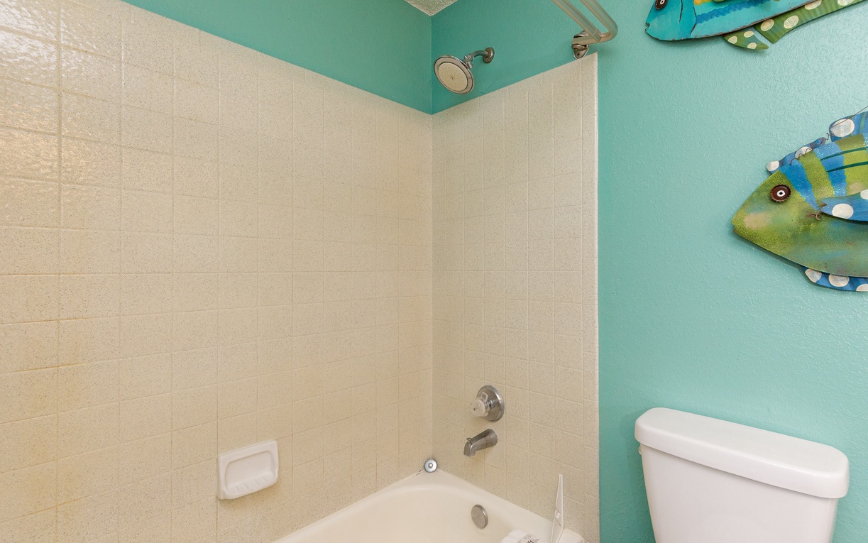 Refresh in your bright turquoise bathroom with tropical fish art and a clean tub-shower combo for easy beach rinse-offs.