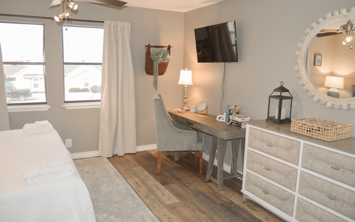 Your serene bedroom workspace features a rustic desk perfect for morning coffee or evening reflection, with warm natural light streaming through large windows.