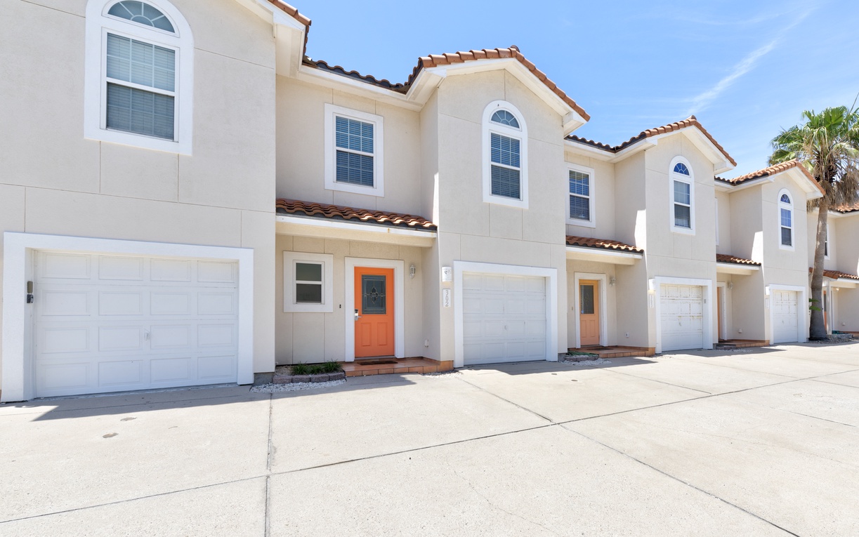 Mediterranean-style townhomes feature terracotta tile roofs and arched windows beneath blue skies, with two designated parking spots for your use.