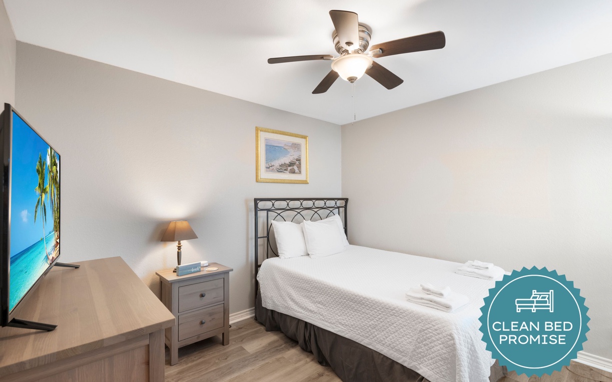 Relax in your peaceful bedroom with ceiling fan, TV, and coastal artwork creating a serene retreat.