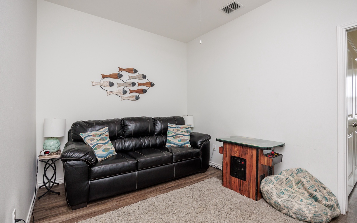 Relax in your cozy living space with comfortable leather seating, playful fish wall art, and a convenient mini arcade table for entertainment.