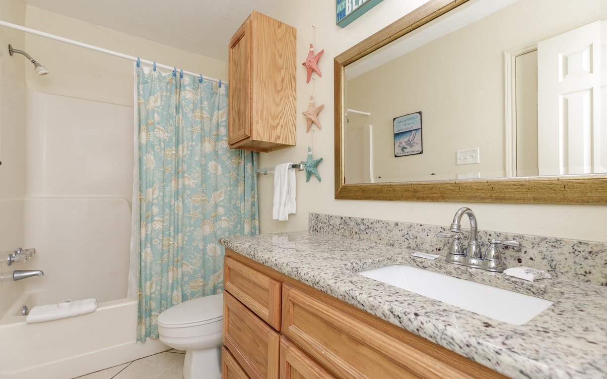 Your coastal-themed bathroom features granite countertops, warm wood cabinetry, and charming beach decor to start your day refreshed.