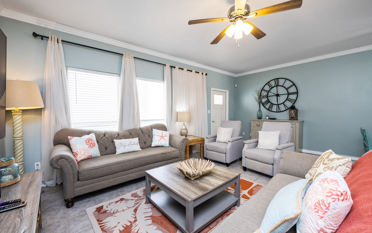 Your peaceful living room invites you to unwind with plush seating and coastal charm beneath gentle ceiling fan breezes.